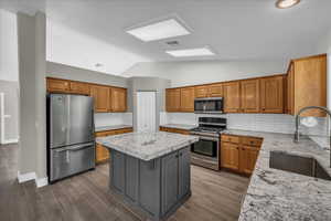 Kitchen with appliances with stainless steel finishes, a sink, a center island, vaulted ceiling, and light stone counters