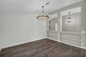 Empty room featuring a chandelier, dark wood-type flooring, baseboards, and built in features