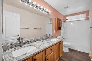 Full bathroom with toilet, double vanity, washtub / shower combination, and wood finished floors