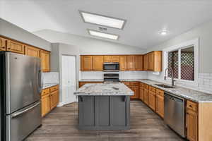 Kitchen with appliances with stainless steel finishes, a sink, lofted ceiling, a center island, and decorative backsplash