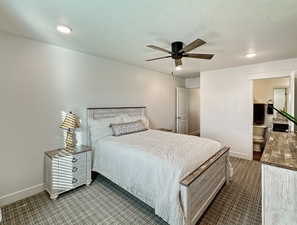 Bedroom with baseboards, dark colored carpet, a ceiling fan, a textured ceiling, and ensuite bath