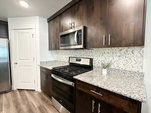 Kitchen featuring appliances with stainless steel finishes, dark brown cabinetry, light wood-style floors, and a textured ceiling
