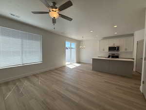 Unfurnished living room featuring ceiling fan, light wood-type flooring, baseboards, recessed lighting, and a chandelier