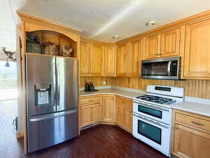 Kitchen with appliances with stainless steel finishes, open shelves, light countertops, dark wood-type flooring, and a textured ceiling
