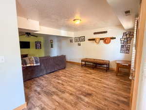 Living room with wood finished floors, ceiling fan, a textured ceiling, and baseboards