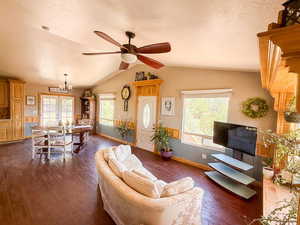 Living area featuring dark wood finished floors, a textured ceiling, lofted ceiling, a ceiling fan, and baseboards