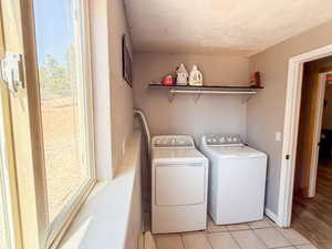Washroom with washing machine and clothes dryer, light tile patterned floors, and a textured ceiling