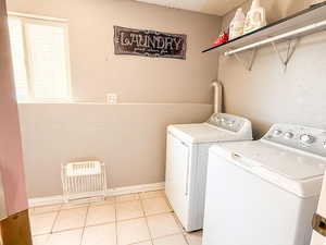 Washroom with washing machine and dryer, light tile patterned floors, and heating unit
