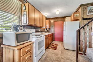 Kitchen featuring white appliances, wood walls, light countertops, brown cabinets, and a textured ceiling