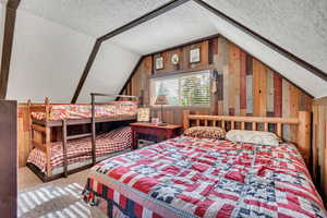 Bedroom with vaulted ceiling, a textured ceiling, wood walls, and carpet floors