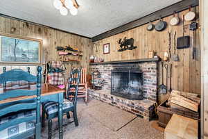 Carpeted living area featuring wood walls, a textured ceiling, and a brick fireplace