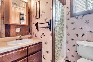 Bathroom with vanity, curtained shower, and wallpapered walls