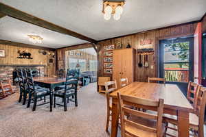 Dining room featuring wooden walls, a textured ceiling, carpet, and beamed ceiling