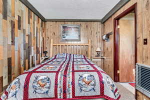 Bedroom with heating unit, wooden walls, and a textured ceiling