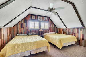 Bedroom with vaulted ceiling, wooden walls, carpet floors, and ceiling fan