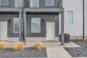 Property entrance with a balcony, board and batten siding, cooling unit, and brick siding