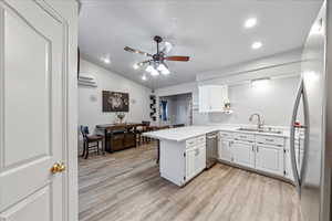 Kitchen featuring appliances with stainless steel finishes, a sink, a peninsula, light countertops, and white cabinetry