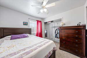 Bedroom featuring a closet, light carpet, ceiling fan, and a textured ceiling