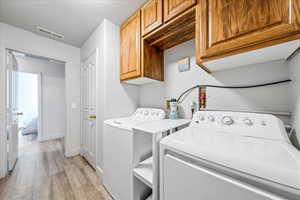 Laundry area featuring cabinet space, washing machine and dryer, light wood-style floors, and baseboards