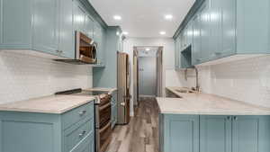 Kitchen with stainless steel appliances, a sink, light wood-style floors, decorative backsplash, and recessed lighting