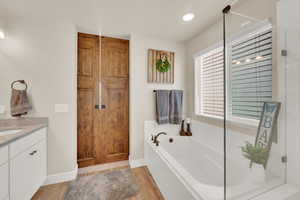 Full bath with wood finished floors, a bath, vanity, baseboards, and an enclosed shower