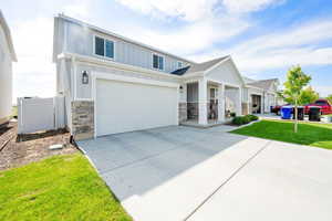 View of front of house featuring stone siding, board and batten siding, concrete driveway, and a front lawn