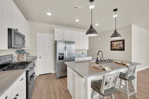 Kitchen with appliances with stainless steel finishes, light wood-type flooring, a sink, a kitchen island with sink, and white cabinets
