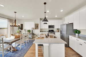 Kitchen with stainless steel appliances, a sink, light wood finished floors, an island with sink, and white cabinets