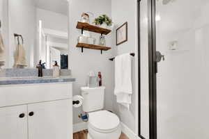 Bathroom with toilet, a stall shower, vanity, wood finished floors, and baseboards