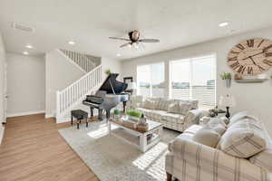 Living area featuring light wood-style floors, ceiling fan, stairs, recessed lighting, and baseboards