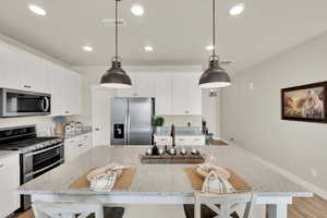 Kitchen featuring stainless steel appliances, a center island, a breakfast bar, white cabinetry, and light stone counters