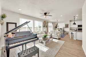 Living room featuring a ceiling fan, light wood-style floors, a textured ceiling, recessed lighting, and baseboards