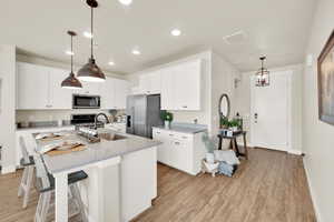 Kitchen with appliances with stainless steel finishes, a sink, light wood-style floors, a center island with sink, and recessed lighting
