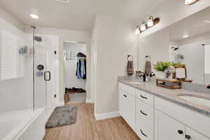 Bathroom featuring a stall shower, double vanity, wood finished floors, a spacious closet, and a bath