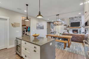 Kitchen with beverage cooler, a fireplace, light wood-style flooring, white cabinetry, and quartz countertops