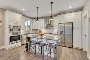 Kitchen with stainless steel appliances, wall chimney range hood, double oven (convection), and a light wood-type flooring, and backsplash up to ceiling