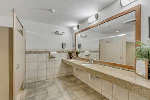 Bathroom featuring tile walls, wainscoting, a textured ceiling, tile patterned flooring, and vanity