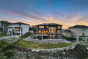Back of house at dusk featuring a yard, stairs, a patio, and a residential view
