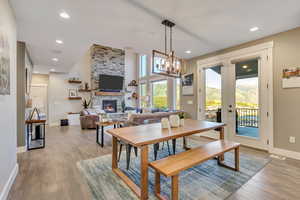Dining area with a stone fireplace, french doors, light wood-style flooring,  and a chandelier