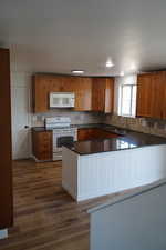 Kitchen with white appliances, a sink, dark wood finished floors, dark countertops, and tasteful backsplash