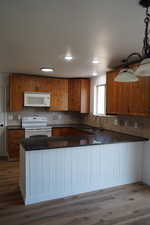 Kitchen featuring white appliances, a sink, brown cabinetry, dark countertops, and wood finished floors