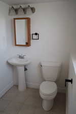 Half bathroom with baseboards, toilet, and tile patterned floors