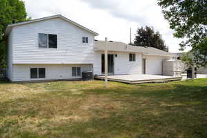 Rear view of property with a deck, a lawn, cooling unit, and roof with shingles