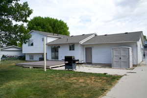 Rear view of property featuring a wooden deck, a yard, a shingled roof, and a patio