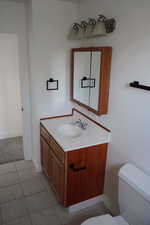 Half bathroom with toilet, vanity, baseboards, and tile patterned flooring