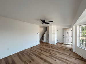 Unfurnished living room featuring wood finished floors, baseboards, ceiling fan, and stairs