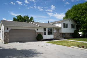 Split level home with brick siding, an attached garage, driveway, a front yard, and a shingled roof