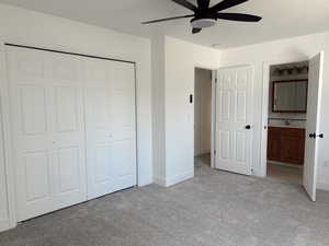 Unfurnished bedroom featuring light carpet, a closet, baseboards, ensuite bathroom, and a ceiling fan