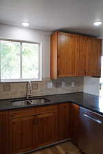 Kitchen with stainless steel dishwasher, a sink, brown cabinetry, and decorative backsplash