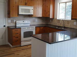 Kitchen with white appliances, a sink, brown cabinets, wood finished floors, and dark countertops